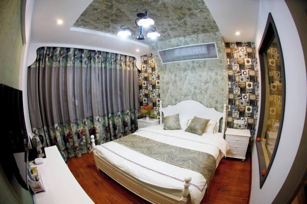 Quarto com cama, cortinas, mesa de cabeceira, cômoda e espelho.