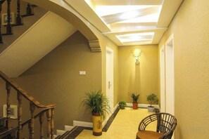 A hallway with a staircase, potted plants, and a chair. - Fallen Bay (Shengsi)