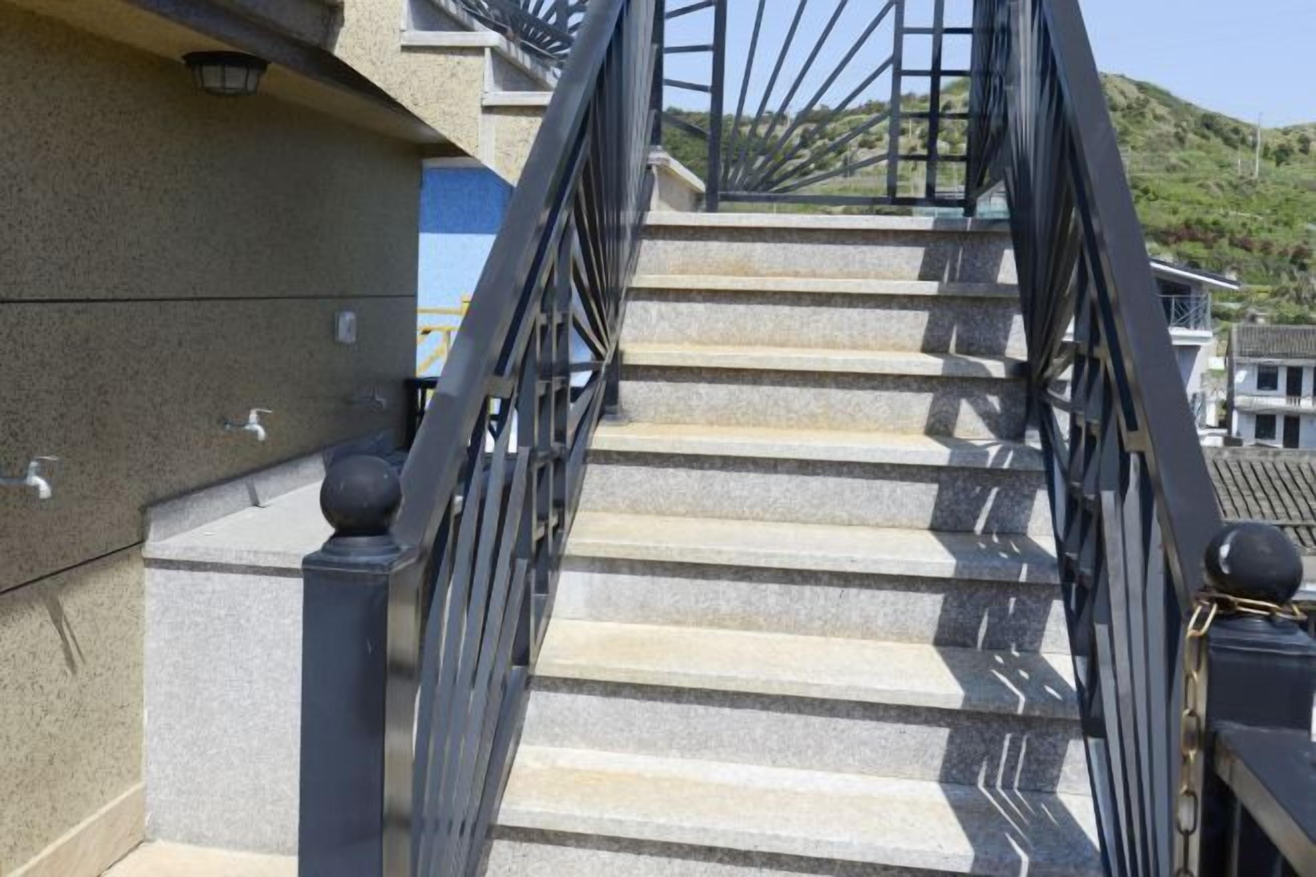 Un escalier extérieur en pierre, agrémenté d’une rampe en métal noir, mène à un bâtiment.