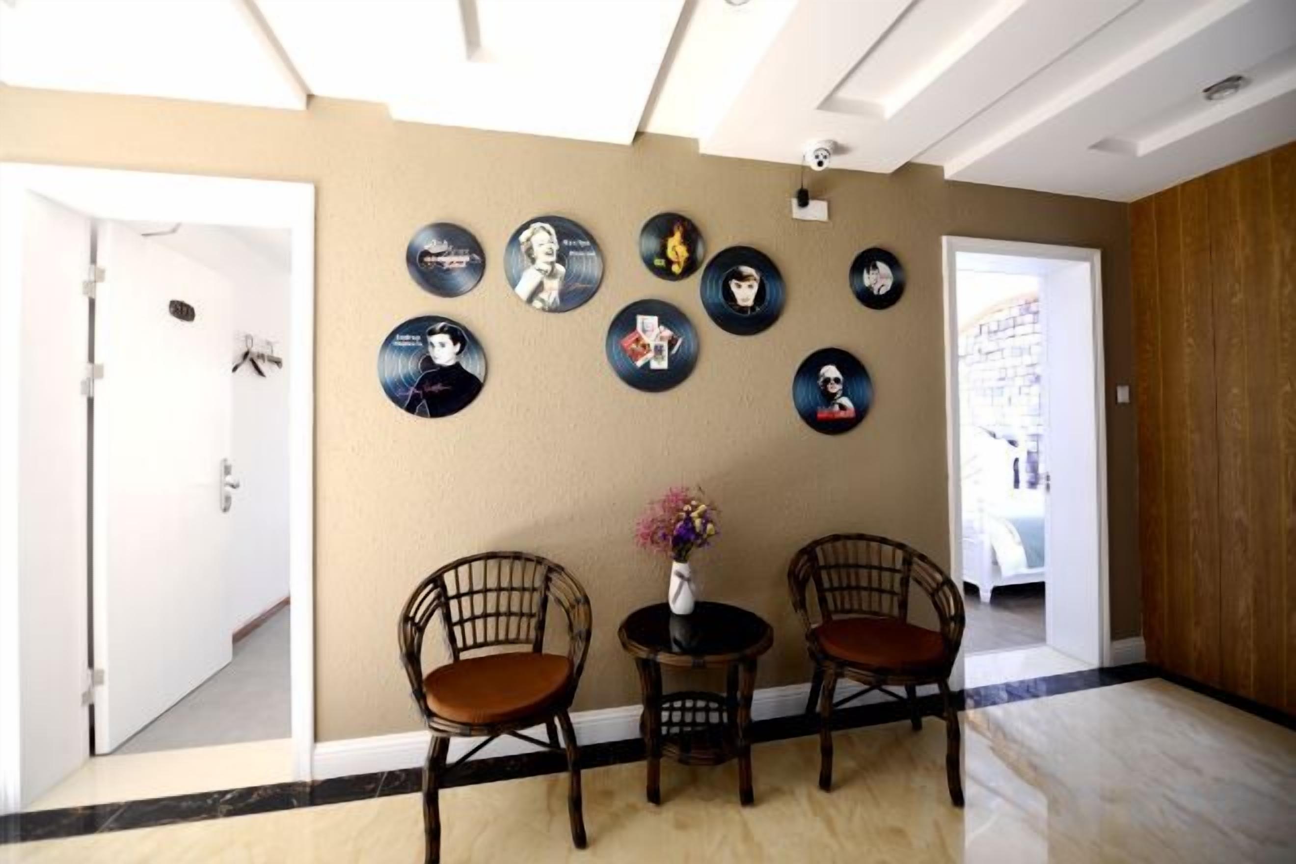 Una habitación con pared color crema, puerta de madera y techo blanco. Hay dos sillas y una pequeña mesa con un florero.