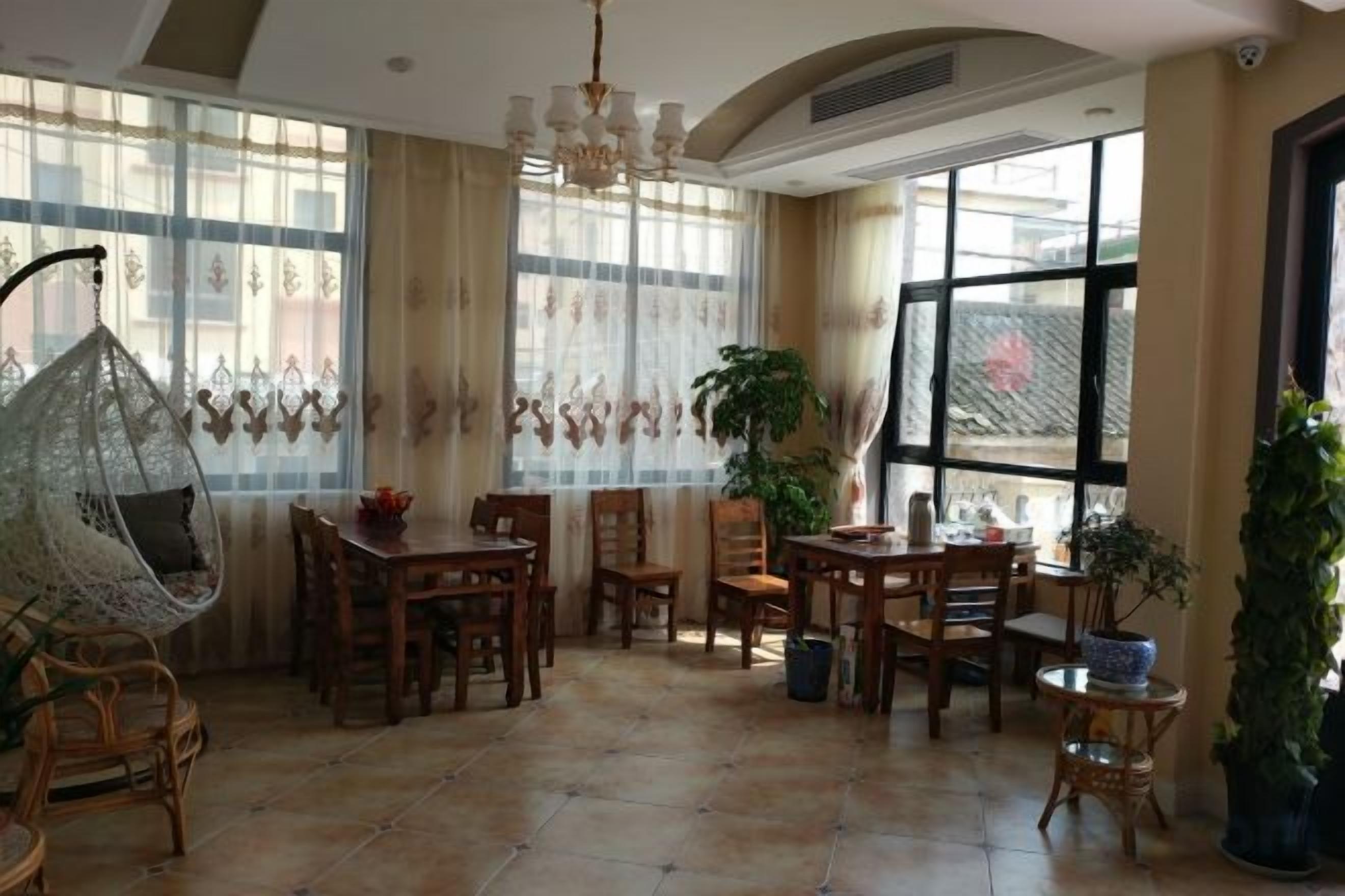 A dining area with wooden furniture, a hanging chair, and large windows with curtains.