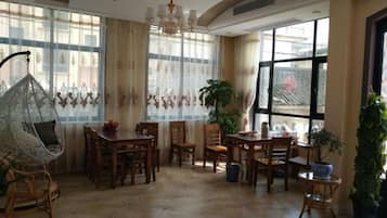 A dining area with wooden furniture, a hanging chair, and large windows with curtains.
