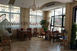 Un comedor con muebles de madera, una silla colgante y ventanas grandes con cortinas.