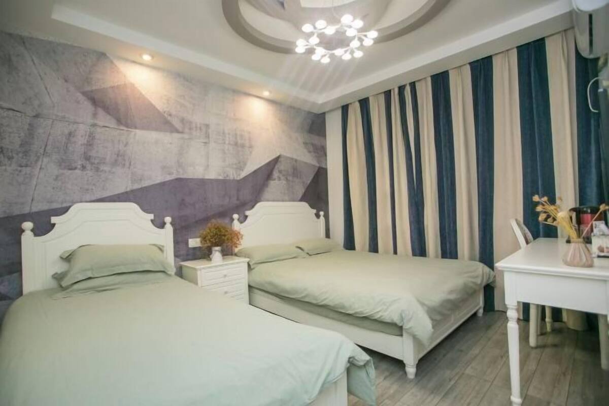 Quarto com duas camas, uma escrivaninha e um lustre moderno.