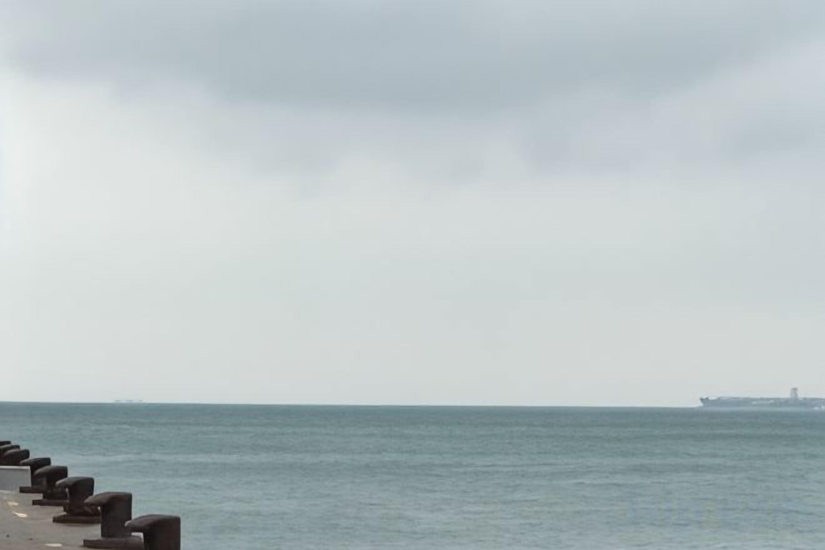 A coastal scene with a row of concrete bollards along the shore and a ship in the distance.