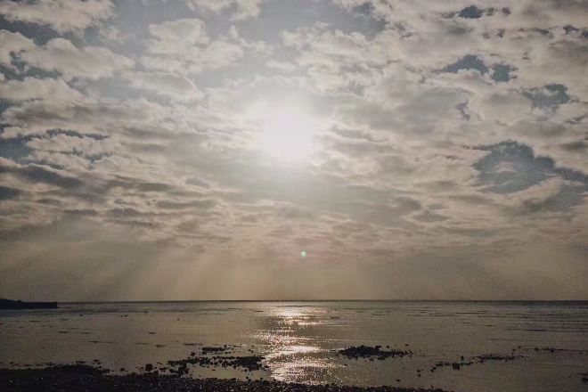 Una playa con cielo nublado y reflejos de sol en el agua.