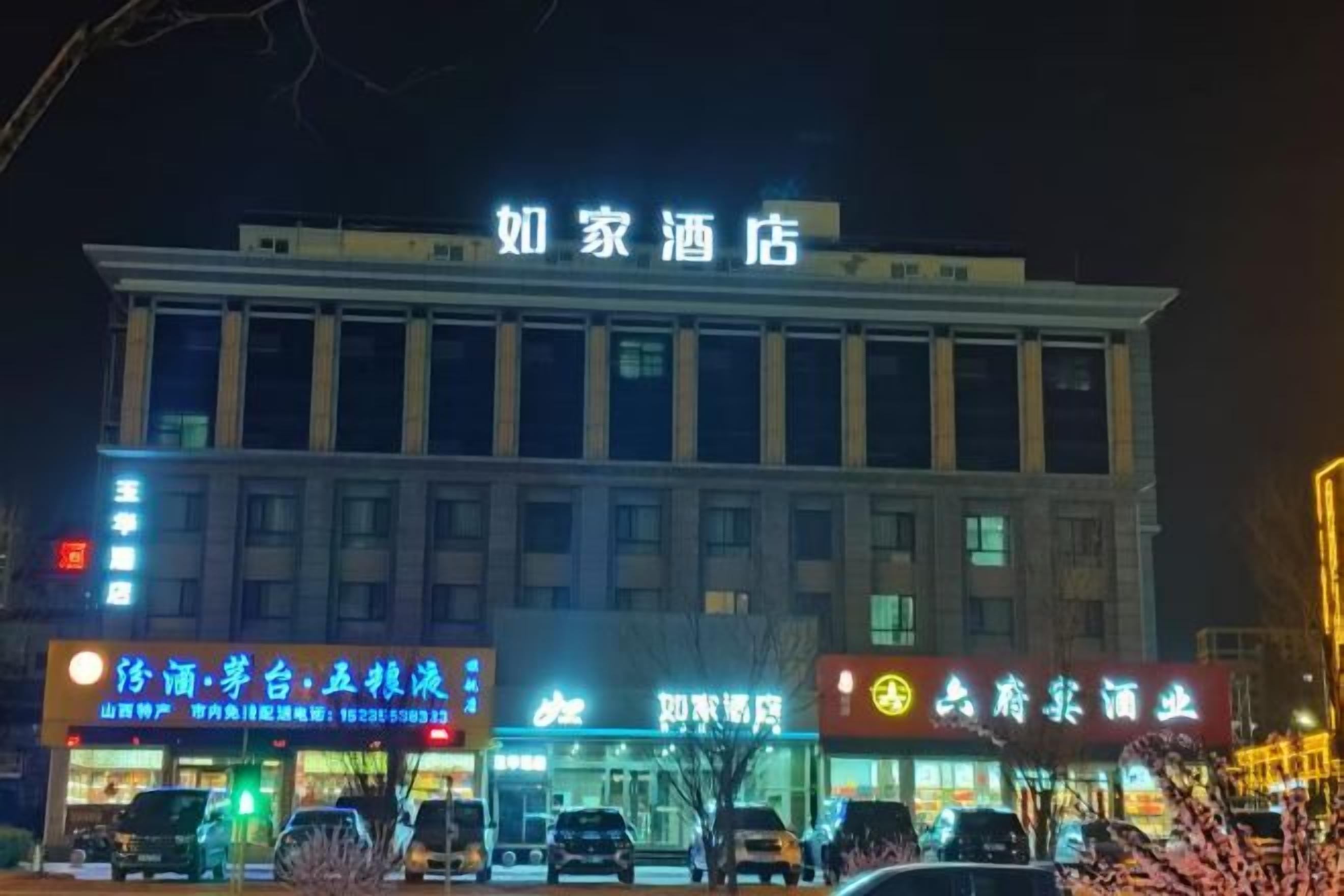 A hotel with a prominent sign, multiple ground-level shops, and a parking area.