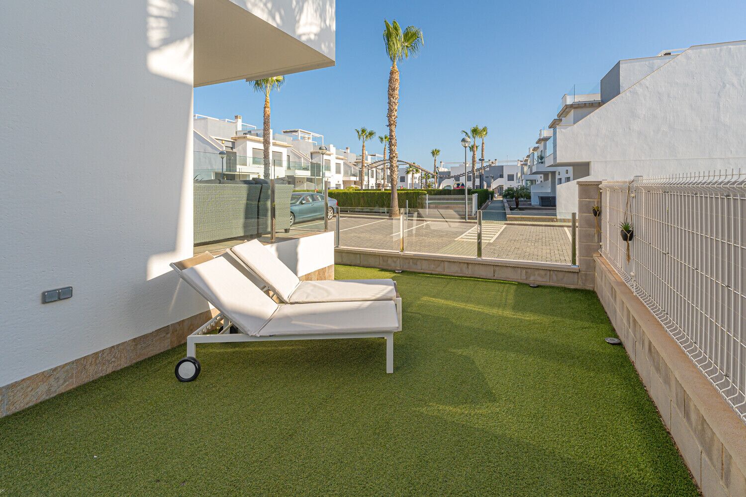 Un área de descanso al aire libre moderna, con una silla lounge blanca, césped artificial y vistas de los edificios circundantes.