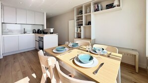 Una cocina moderna con armarios blancos, una mesa de comedor de madera dispuesta con platos y vasos azules, y una estantería empotrada con libros y objetos decorativos.