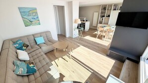 Una sala de estar moderna con un sofá seccional, un comedor y una cocina al fondo.