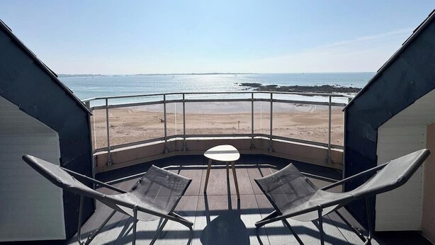 Un balcón con dos sillas y una mesa, con vista a la playa y al mar.