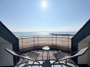 Un balcon avec deux chaises et une table, donnant sur une plage et la mer.