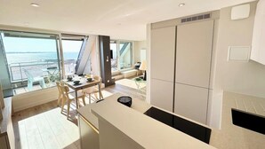 Una cocina moderna con una isla grande, un comedor con vistas y un amplio salón con un ventanal que da a la ciudad.