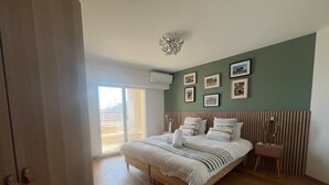Un dormitorio con una cama grande, suelo de madera, pared de acento verde y vistas a través de una puerta corredera.