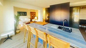 Una cocina moderna con encimera de mármol, pileta integrada y muebles de cocina oscuros. Hay sillas de mimbre y una pequeña mesa de comedor.