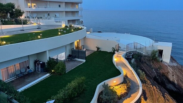 Un hotel moderno con un camino curvo, un jardín en la azotea y vistas al mar.