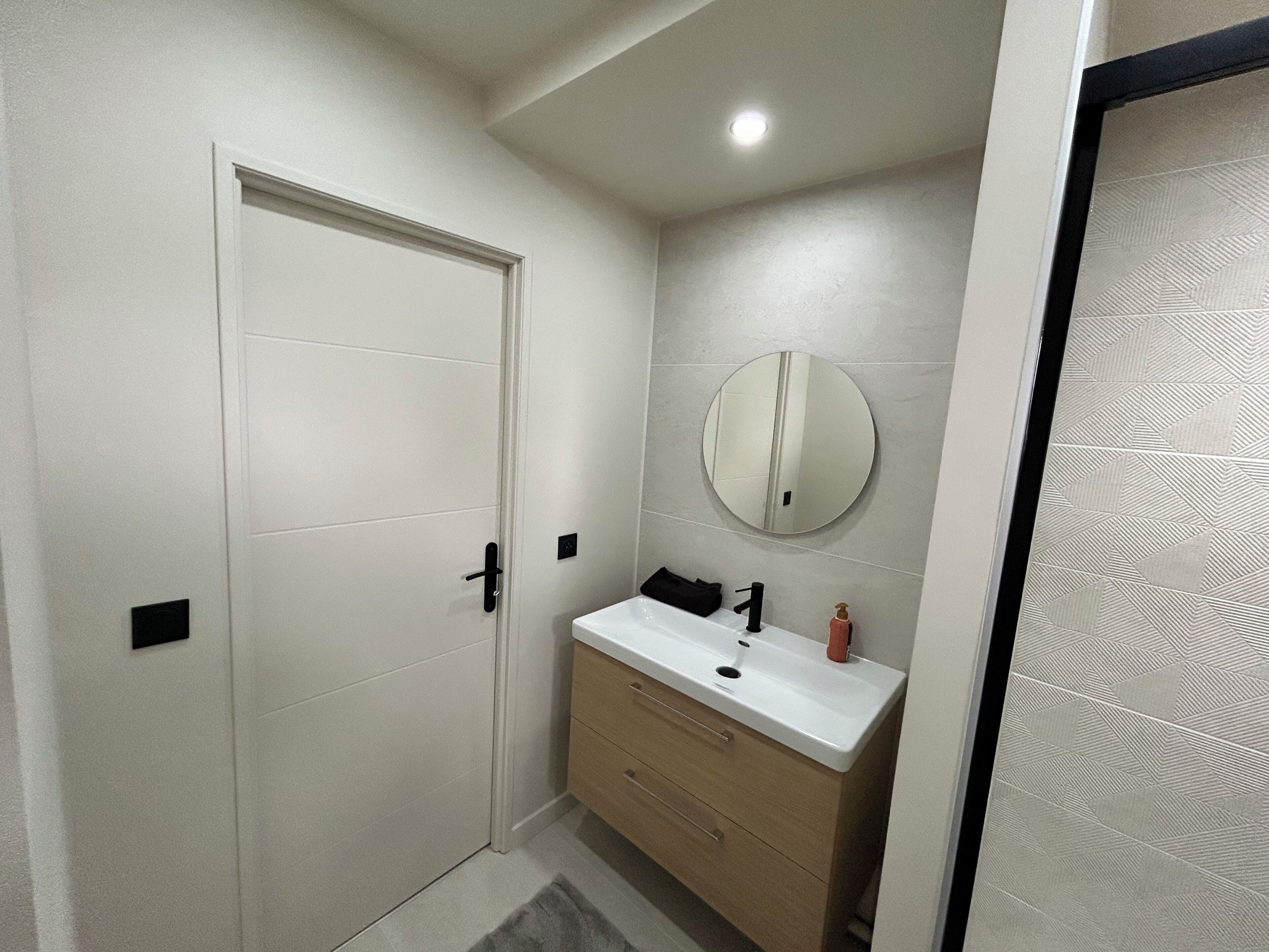 A bathroom with a white door, a round mirror, a sink, and a towel rack.