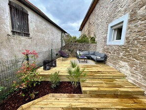Un patio con cubierta de madera, pared de piedra, un sofá gris y una mesa peque ña.