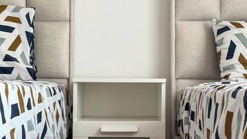 Une chambre à coucher avec deux lits, chacun agrémenté de draps à motifs, une commode blanche placée au centre et une tête de lit rembourrée.