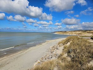 A beach with a sandy shore, grassy dunes, and a clear sky with clouds.