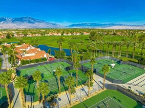 Une vue aérienne d’un terrain de golf avec plusieurs courts de tennis, entouré de bâtiments résidentiels et de palmiers.