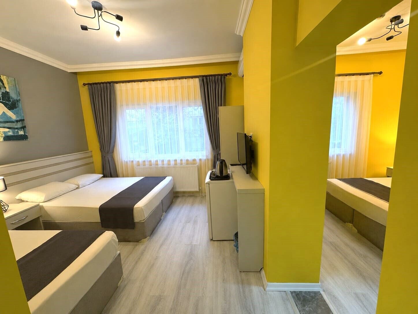 Ett hotellrum med två sängar, ett skrivbord, en TV och ett fönster med gardiner.