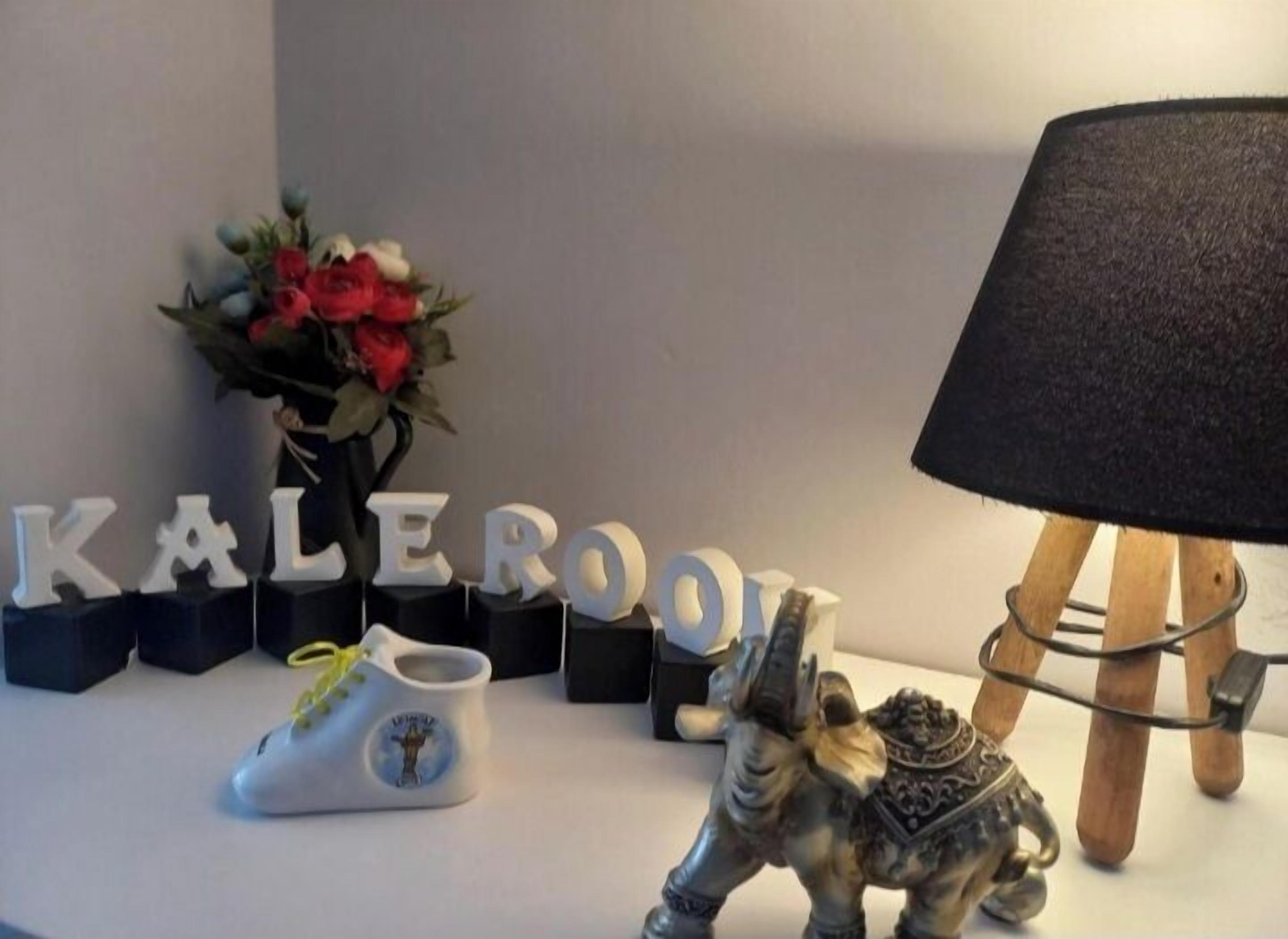 A decorative setup with the word "KALEROO" spelled out in letters, a small figurine of a horse, a lamp, and a vase with flowers.