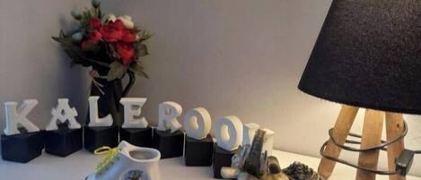 A decorative setup with the word "KALEROO" spelled out in letters, a small figurine of a horse, a lamp, and a vase with flowers.