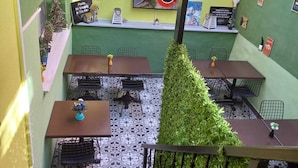 Un espace extérieur aménagé avec des tables et des chaises, un mur végétal orné de silhouettes d’oiseaux, une pancarte de bienvenue et une autre interdisant de fumer.