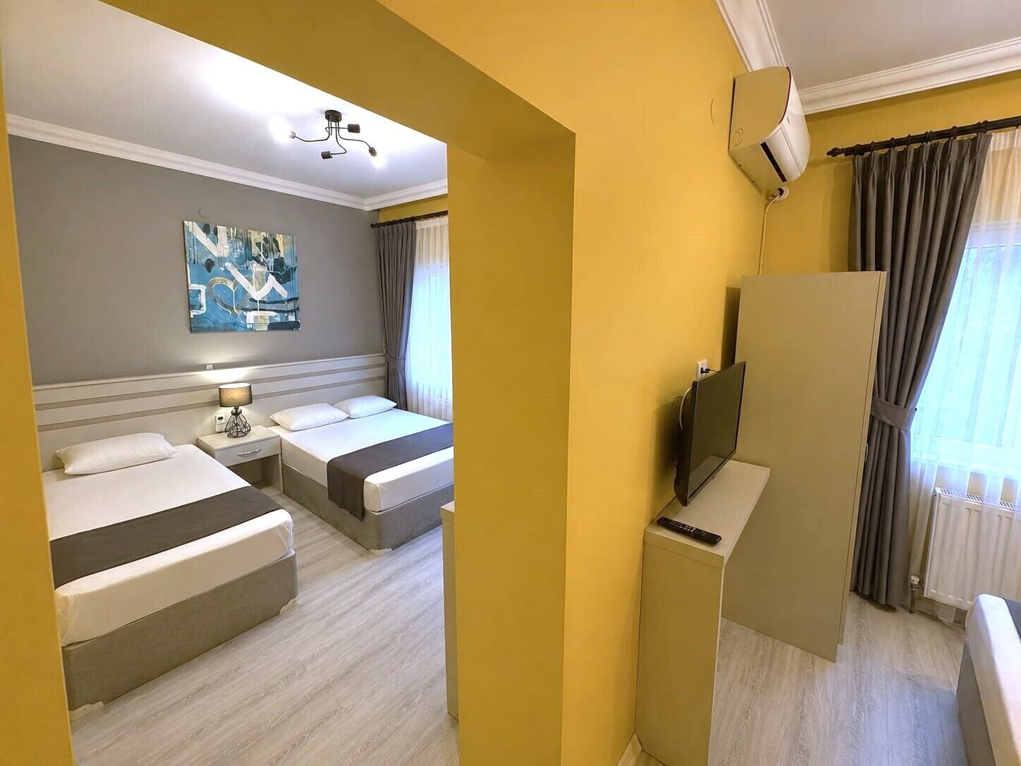A hotel room with two beds, a flat-screen TV, a painting on the wall, and a ceiling light.
