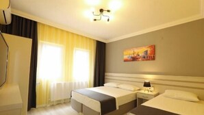 Une chambre d’hôtel avec deux lits, une table de chevet avec une lampe, un tableau au mur et une fenêtre avec des rideaux.