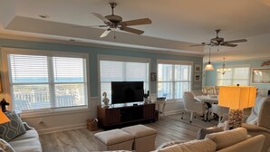 Ein Wohnzimmer mit Fernseher, Sofas, einem Essbereich und Deckenventilatoren.
