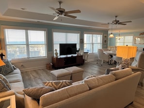 A living room with a TV, sofas, a dining area, and ceiling fans.
