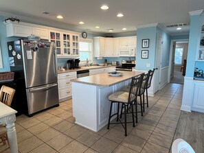 A kitchen with a stainless steel refrigerator, white cabinets, a granite countertop island, and a dining area with bar stools.
