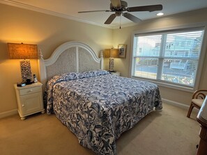 A bedroom with a bed, a nightstand, a lamp, a ceiling fan, and a window with blinds.