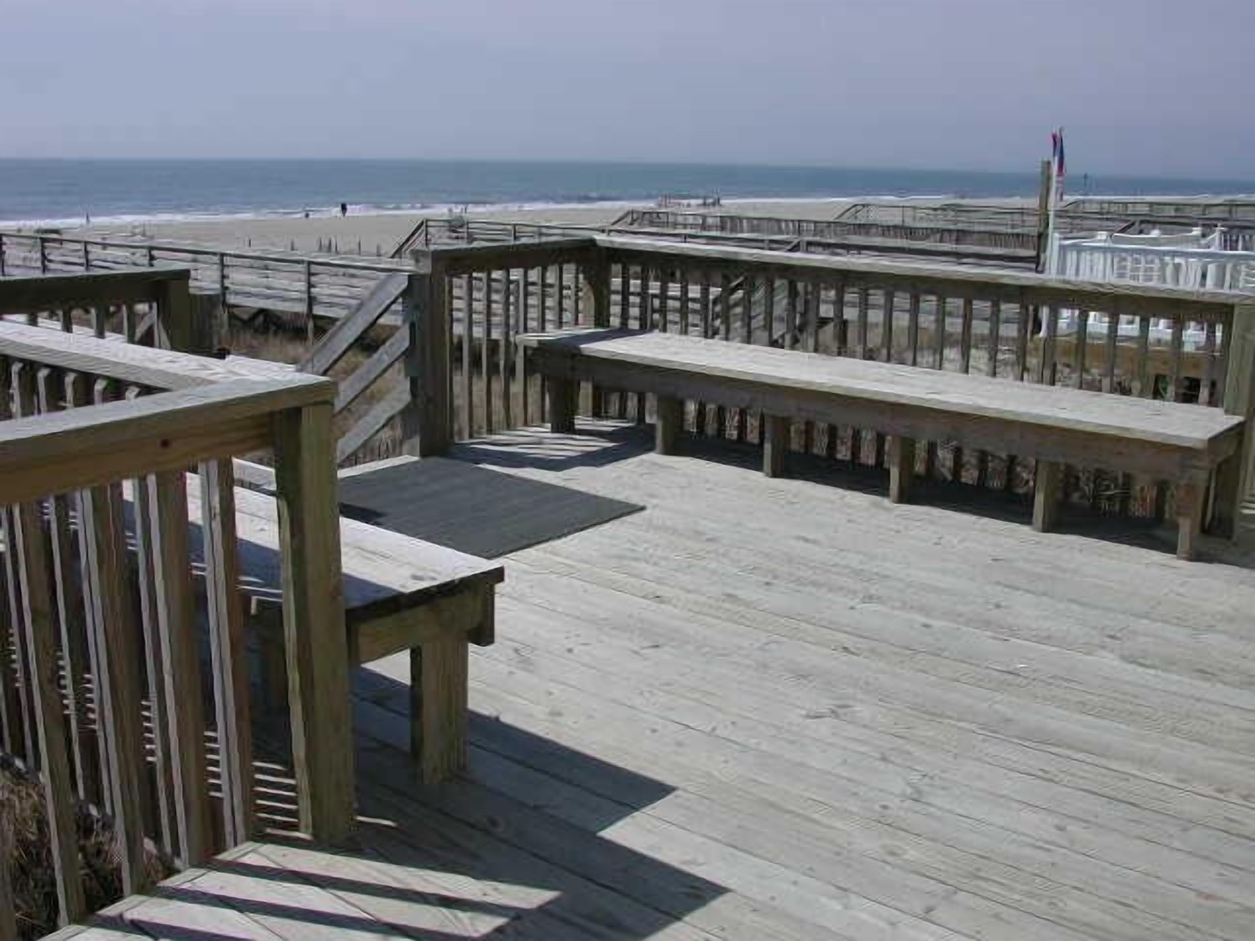 A wooden boardwalk with benches overlooking the beach.