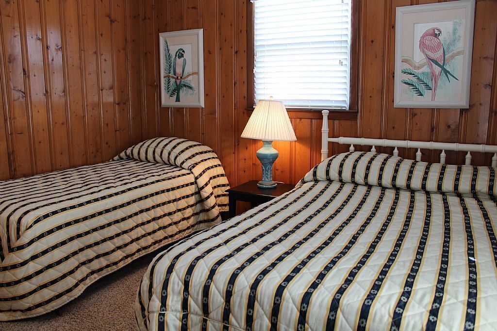 Ein Zimmer mit zwei Betten, Holzwänden, einer Lampe und zwei gerahmten Bildern.