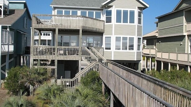 A multi-story beachfront house with a wooden deck and a staircase leading to the upper levels. - Spacious Oceanfront Retreat -Steps to Sand & Pool Access! By Williamson Realty (Ocean Isle Beach)