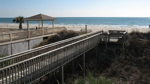 A wooden boardwalk leading to a beach with a gazebo and a small structure. - Spacious Oceanfront Retreat -Steps to Sand & Pool Access! By Williamson Realty (Ocean Isle Beach)