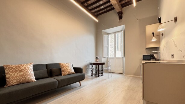 Uma sala de estar moderna com sofá, uma mesinha e uma cozinha com bancada e armários.