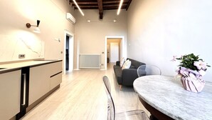 Uma cozinha moderna com bancada de mármore, uma sala de jantar com mesa redonda e uma sala de estar com sofá e planta em vaso.