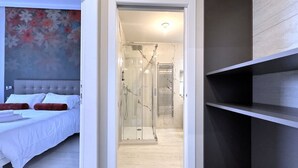 Quarto moderno com cama, área de chuveiro e corredor que leva a um banheiro.