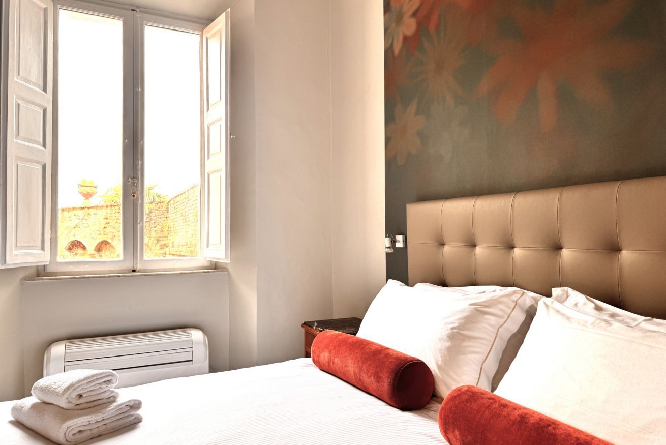 Una habitación de hotel con una cama, una ventana, un radiador y una pared con estampado floral.