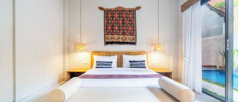 A modern bedroom with a large bed, two bedside tables with lamps, a patterned tapestry, and a view of a swimming pool.