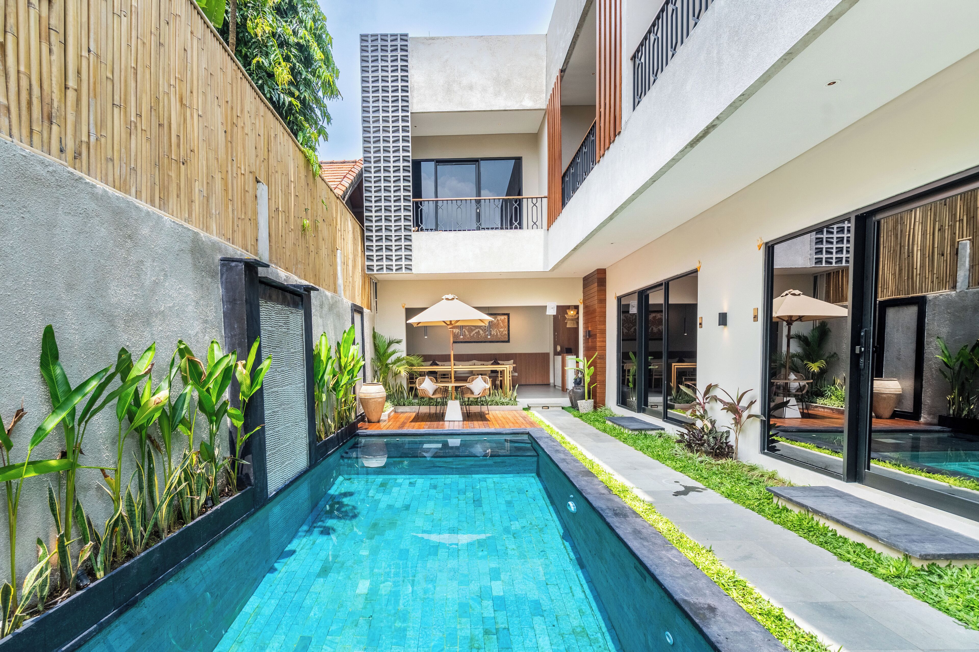 A modern outdoor pool area with a wooden fence, a dining area with outdoor furniture, and a building with large windows and balconies.