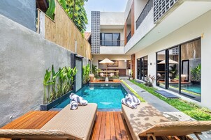 A modern outdoor pool area with wooden loungers and a dining set.
