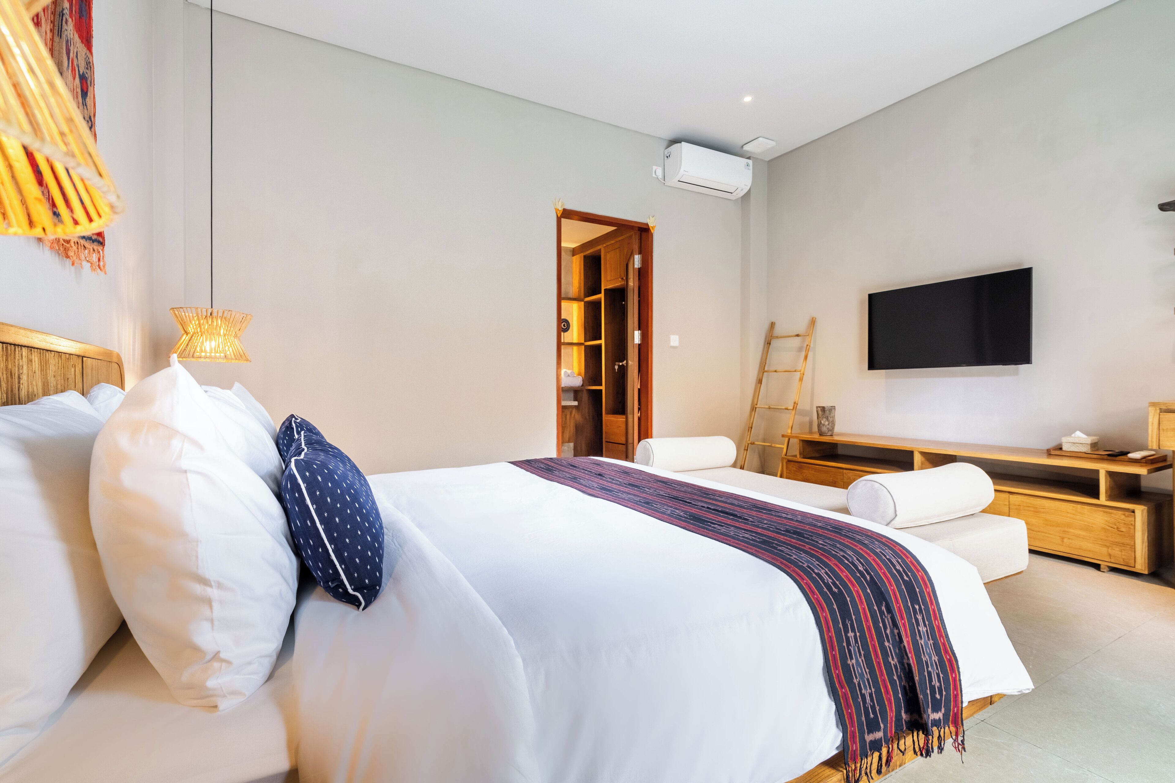A modern hotel room with a large bed, a TV mounted on the wall, a wooden desk, and a wardrobe.