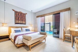 A modern bedroom with a large bed, a desk, and a view of a pool.