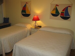 A hotel room with two beds, a nightstand with a lamp, and sailboat wall art. - Oceanfront spacious Condo w/ Stunning Views & Pool Access By Williamson Realty (Ocean Isle Beach)