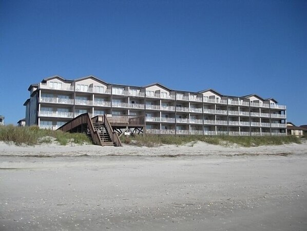 A multi-story hotel with balconies, located on a beach with a wooden walkway leading to the entrance. - Oceanfront spacious Condo w/ Stunning Views & Pool Access By Williamson Realty (Ocean Isle Beach)